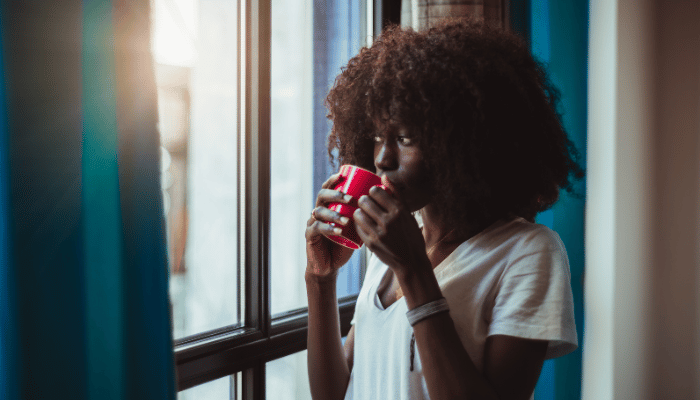 woman looking out of a window sipping a cup of tea