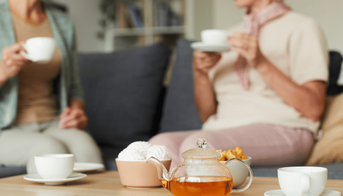image of people enjoying a cup of tea in the background with a pot of tea in focus