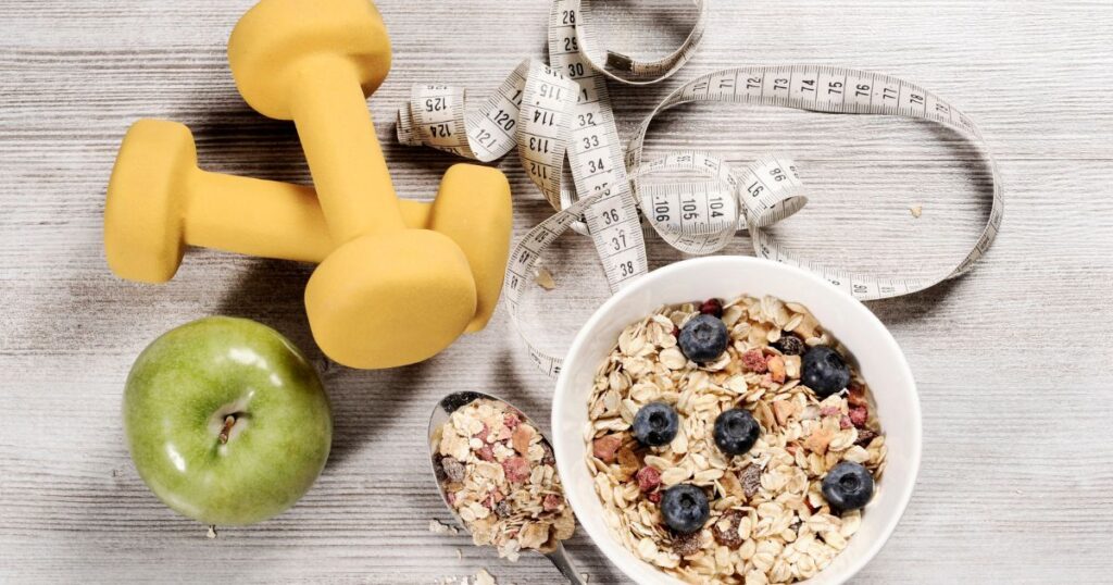 healthy lifestyle bowl of granola, weights, apple and tape measure 