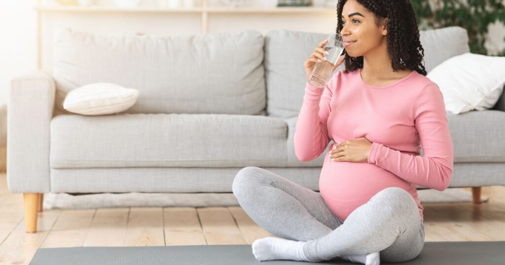 Young black pregnant woman drinking water after training